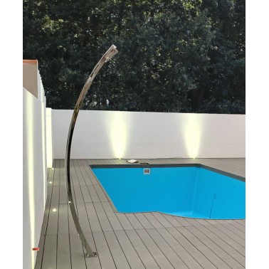 Bazénová sprcha una z leštěné oceli na dřevěné podlaze u venkovního bazénu obklopeného bílou zdí