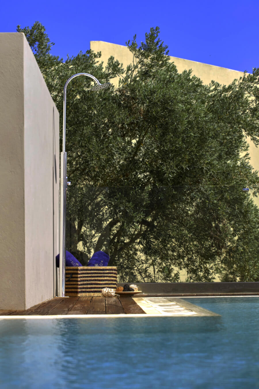 Giove nerezová sprcha z leštěného nerezu umístěná na dřevěné podlaze u venkovního bazénu u rodinné vily v pozadí stromy