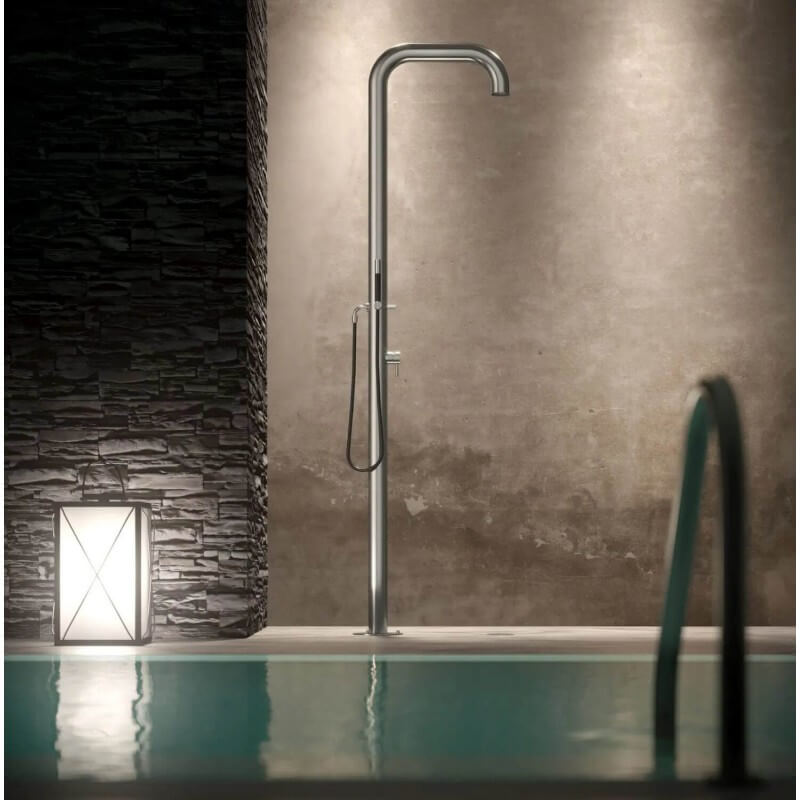 Venkovní sprcha na studenou vodu s ruční sprchou a integrovanou  hlavicí u bazénu v přítmí, osvícena lucernou.